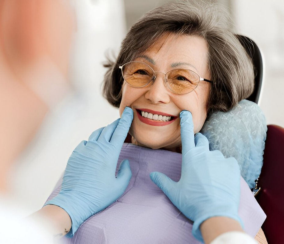 Elderly woman in dental chair smiling as dentist adjusts her dentures