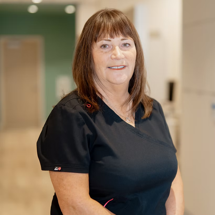 Smiling dental team member in black scrubs standing in a modern clinic hallway